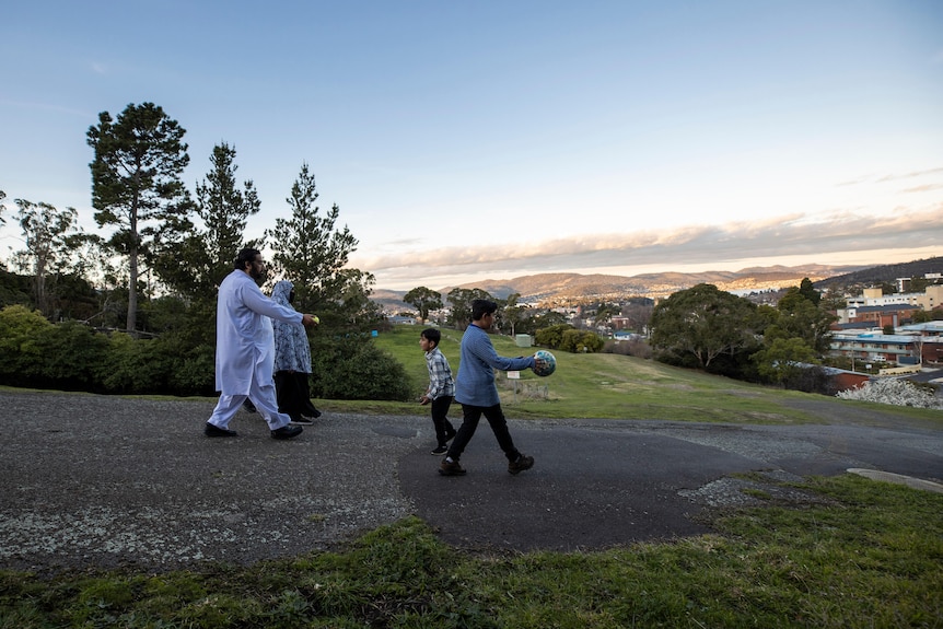 A family walk down a hill while playing with two balls.