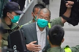 A man in a suit is surrounded by police wearing khaki uniforms, with all people pictured wearing disposable face masks.