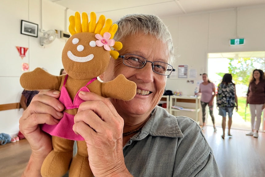 Woman smiles holding doll with smiley face