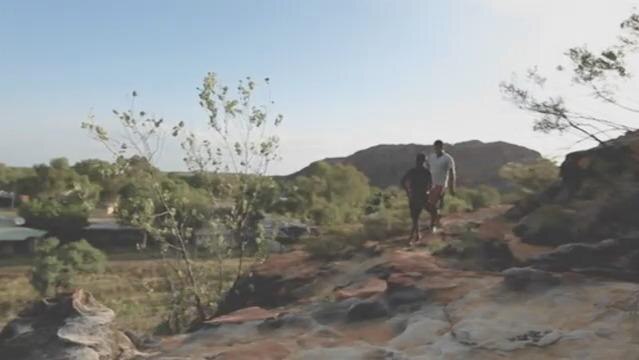 Two men walk though an outback landscape
