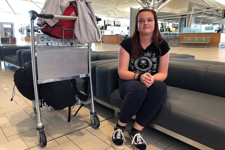 Grace Hoyle sits on a seat at the Brisbane international airport terminal with a luggage trolley.
