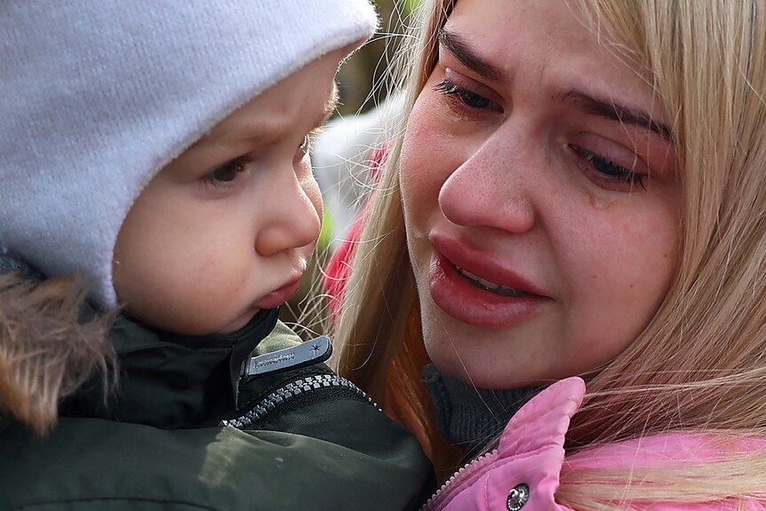 A crying woman holds a young child wearing a beanie.