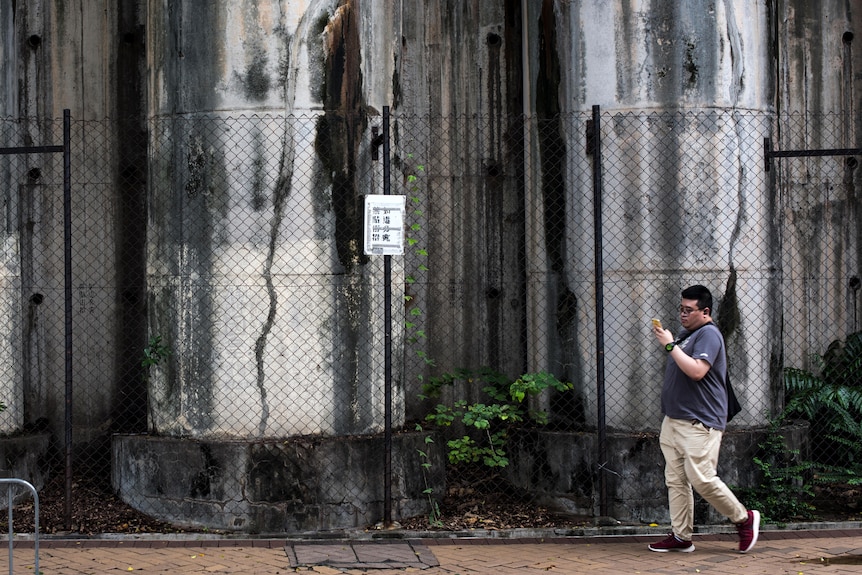 A photo of three concrete pillars with a man walking past looking at his phone.