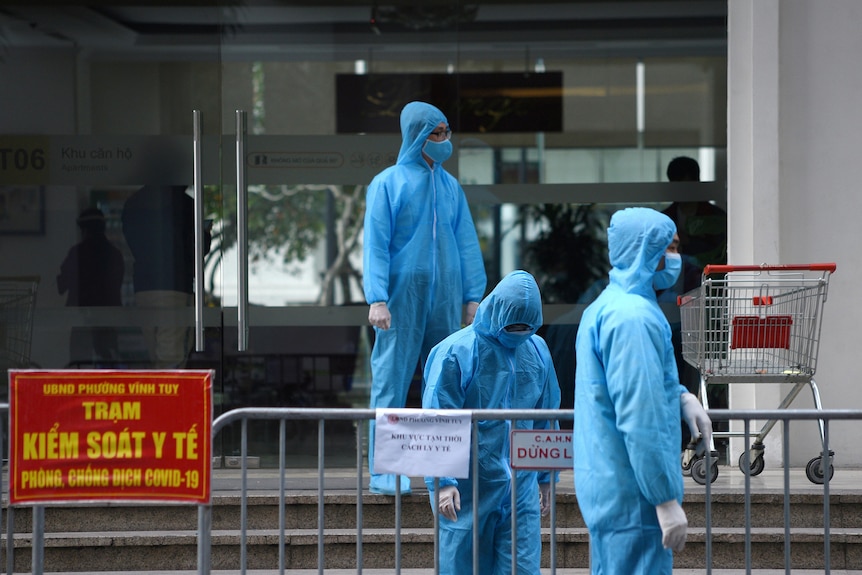 Medical workers in protective suits stand outside a quarantined building in Hanoi