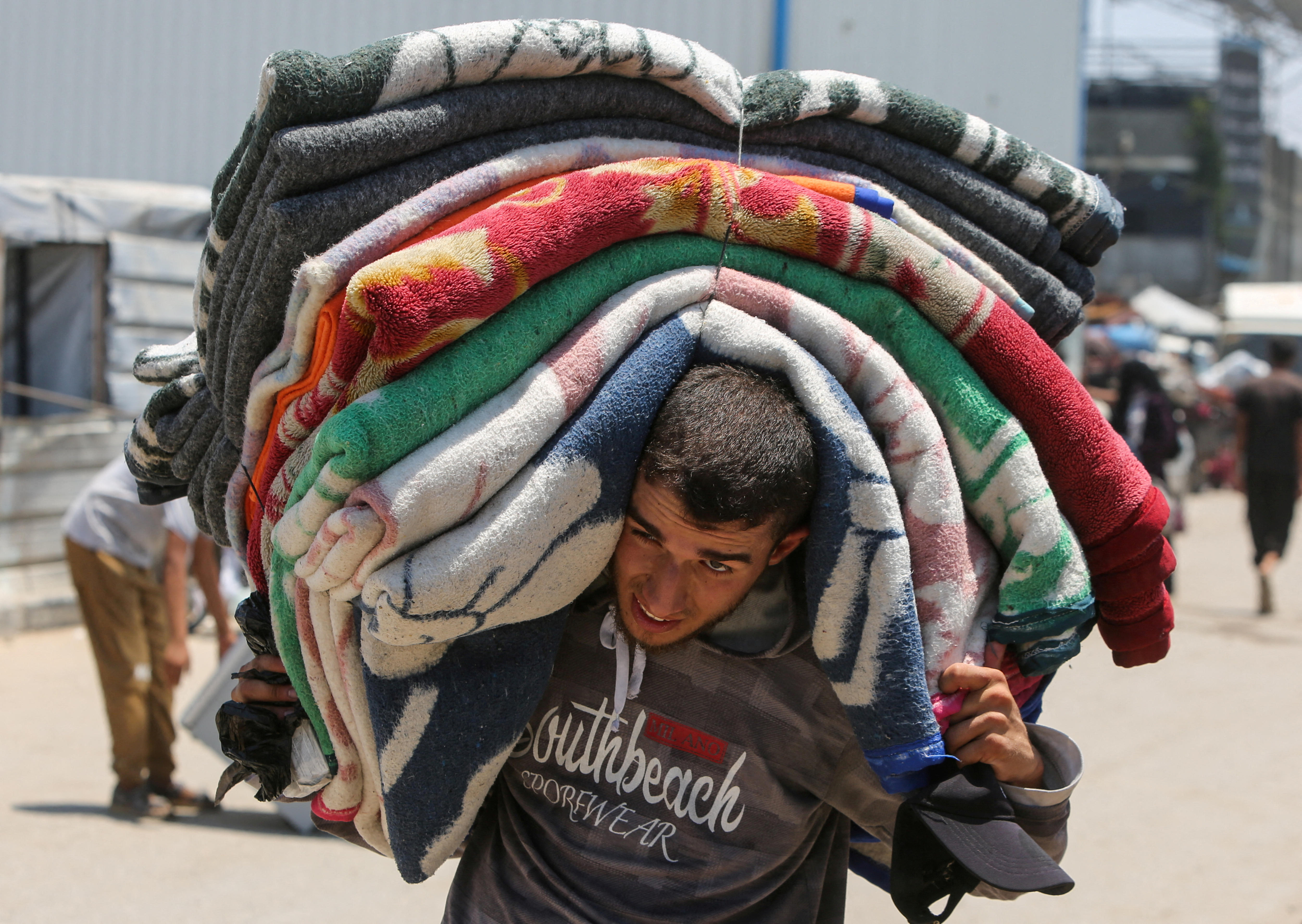 A young man carrying sheets on his back down a dirt road