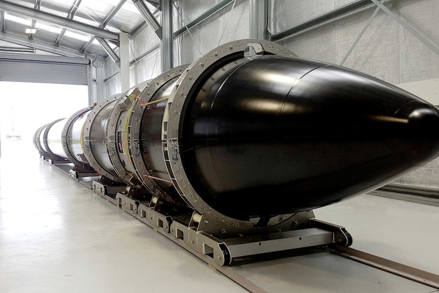 A black rocket fastened onto tracks inside a hanger.