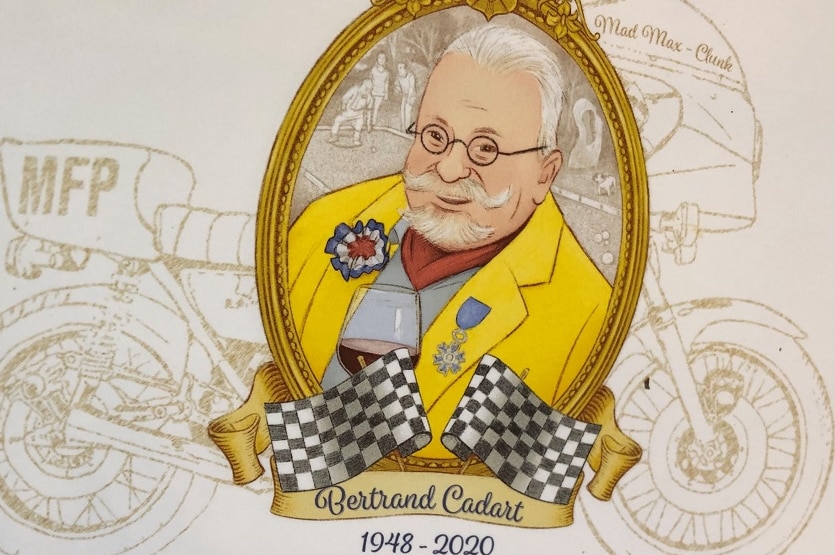 Plaque with painting of Bertrand Cadart holding red wine with yellow jacket, with a motorbike outline behind him.