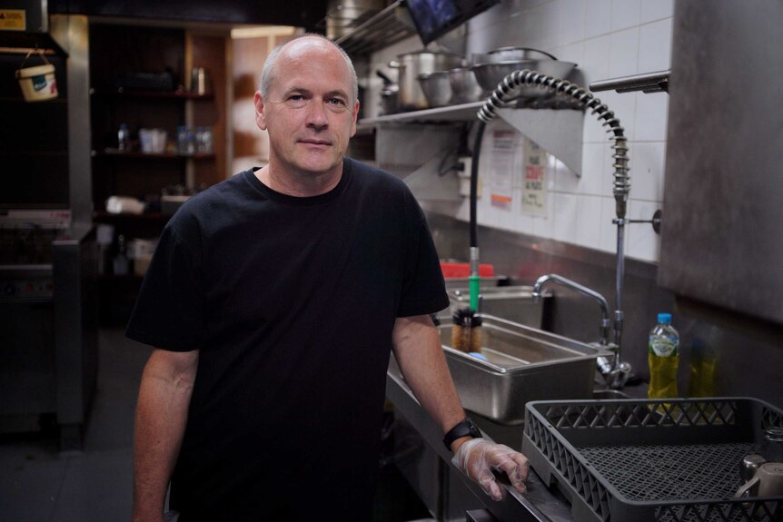 Former pilot Matt Purton stands at the sink in the kitchen of the cafe where he now works.