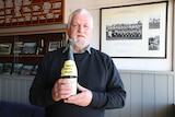 A man holds a dusty bottle of champagne in front of old football photos.