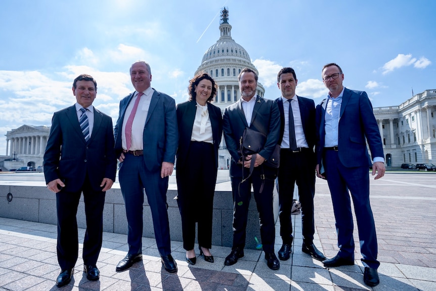 The six politicians stand in front of the US Capitol building.