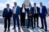The six politicians stand in front of the US Capitol building.