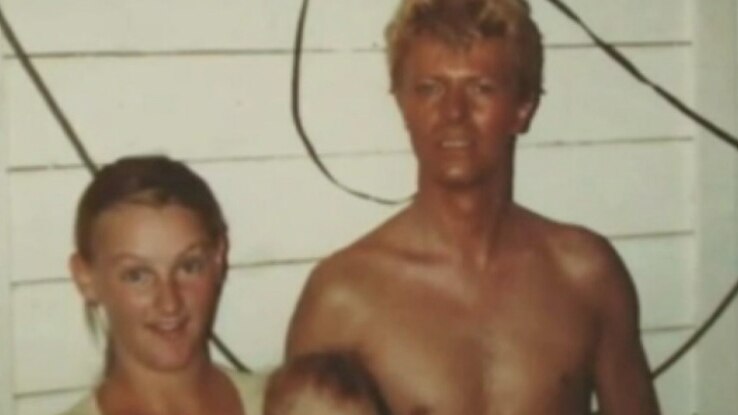 David Bowie stands shirtless, posing with a Carinda local woman and her baby for a photo.