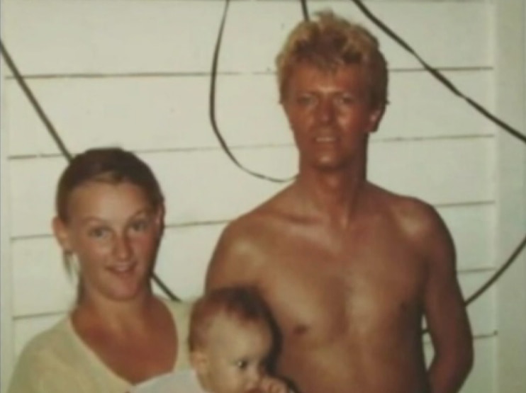 David Bowie stands shirtless, posing with a Carinda local woman and her baby for a photo.