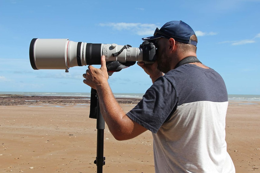 Birdwatcher Marc Gardiner looking into a long camera lens pointed out to sea.