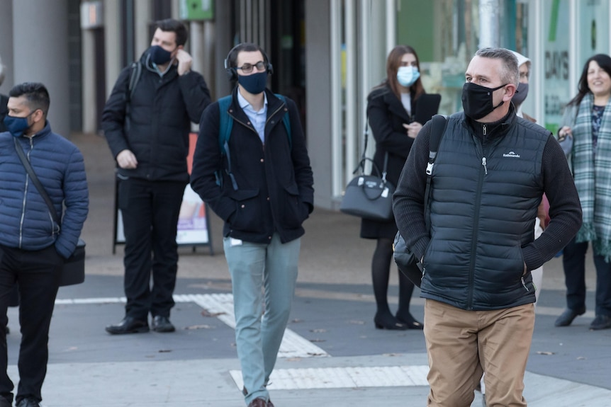 Various men walk through Canberra wearing facemasks