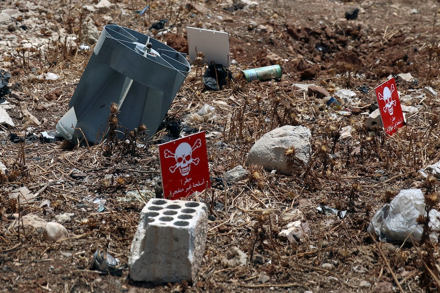 Bomb remains in dirt next to small signs with skull and crossbones on them. 