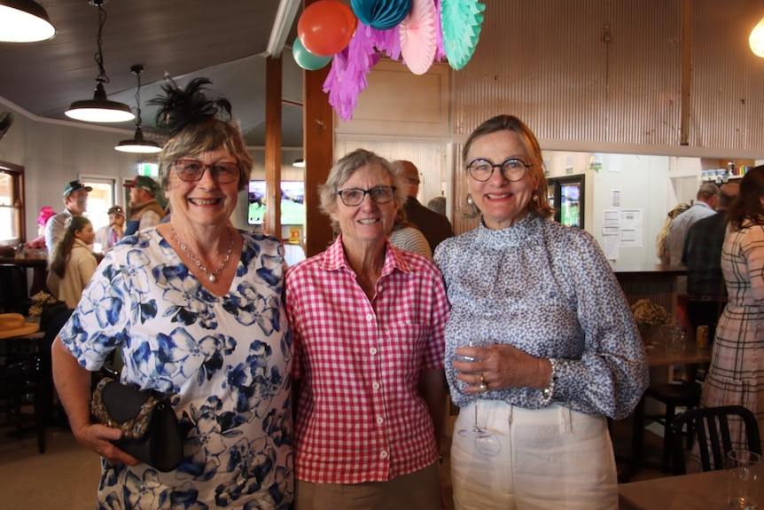 Three women dressed for race day stand arm in arm at the Toompine Pub.