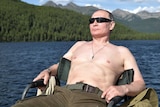 Vladimir Putin leans back in a chair near a lake as the sun hits his shirtless torso.