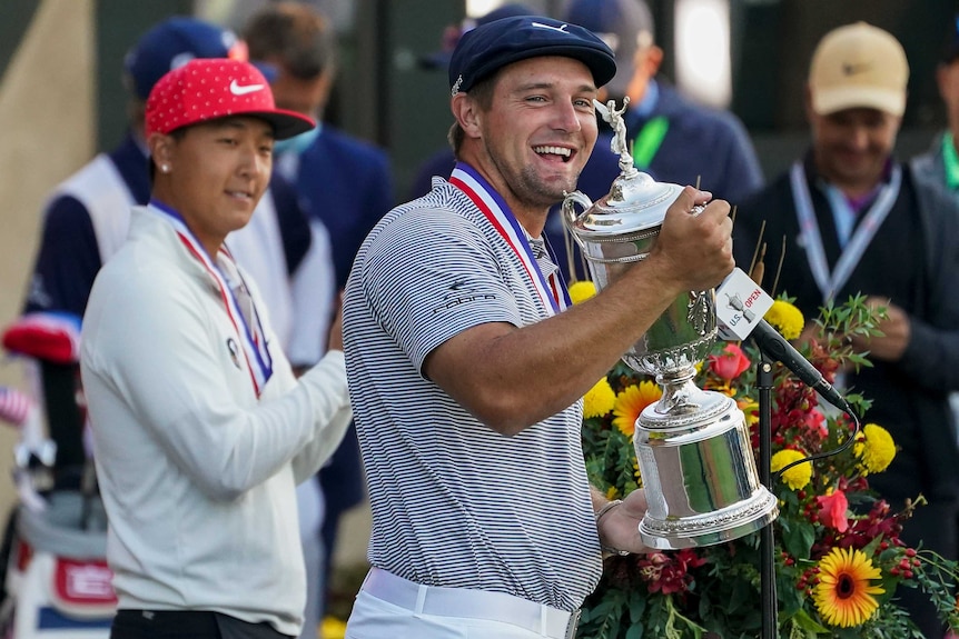 Bryson DeChambeau smiles and looks to the camera holding the US Open trophy