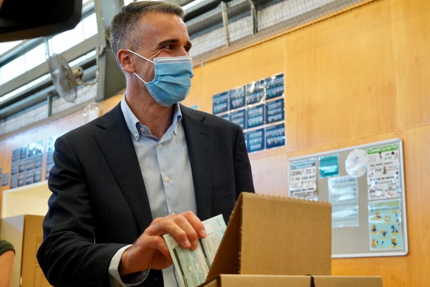 A man putting a ballot in a brown box
