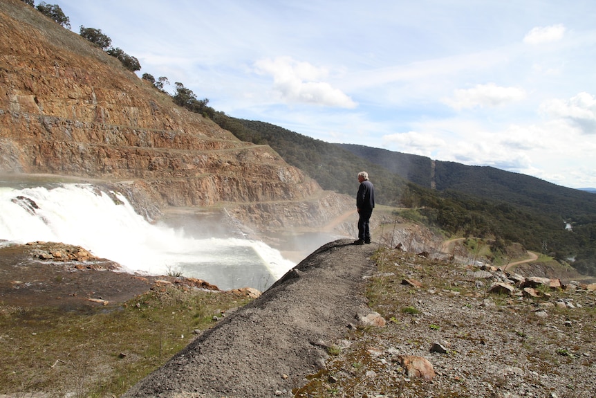 A man stands near a flooded dam spillway.