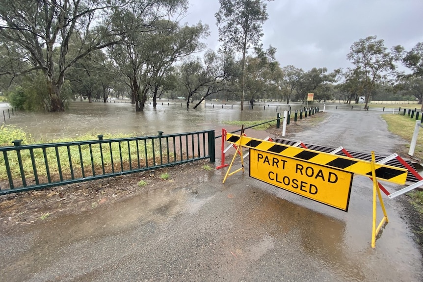 A flooded road with a yellow road closed sign in the foreground.