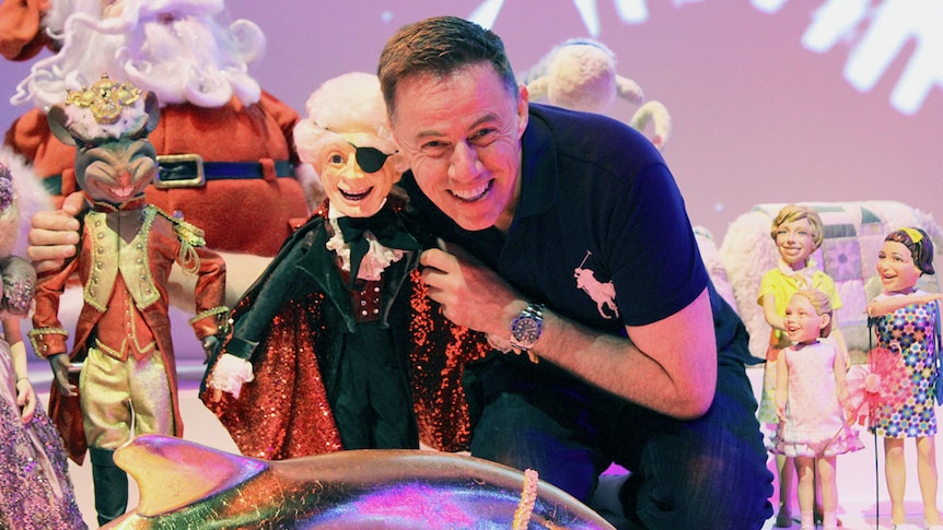 John Kerr puts his arms around a model of a smiling magician with an eyepatch.