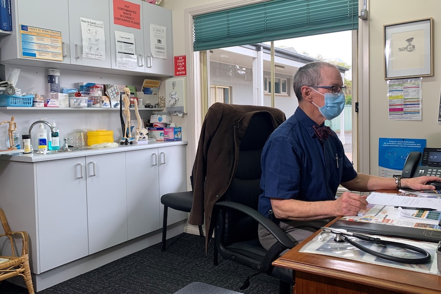 Man wearing face mask at a desk, looking at a computer