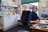 Man wearing face mask at a desk, looking at a computer