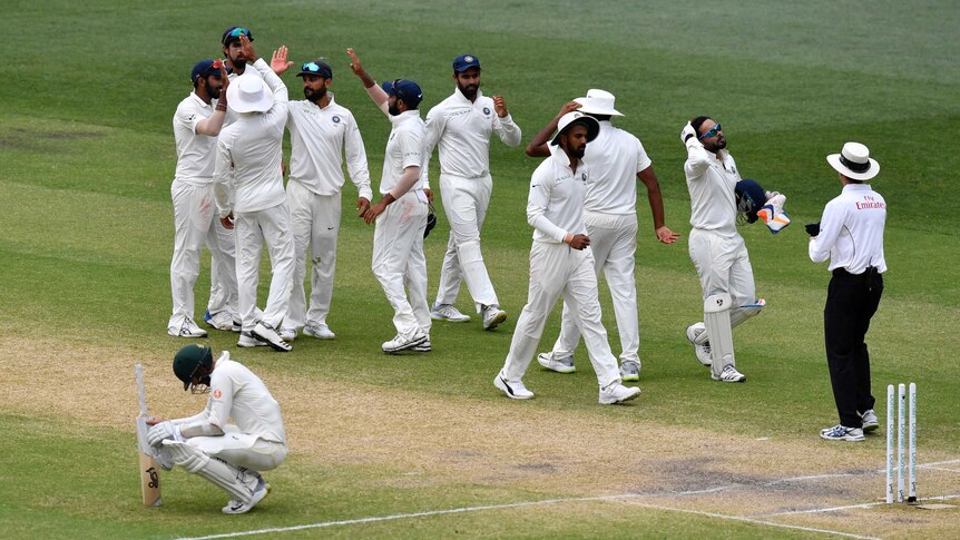 Indian cricketers high-five each other as Australian batsman Nathan Lyon drops to his haunches.