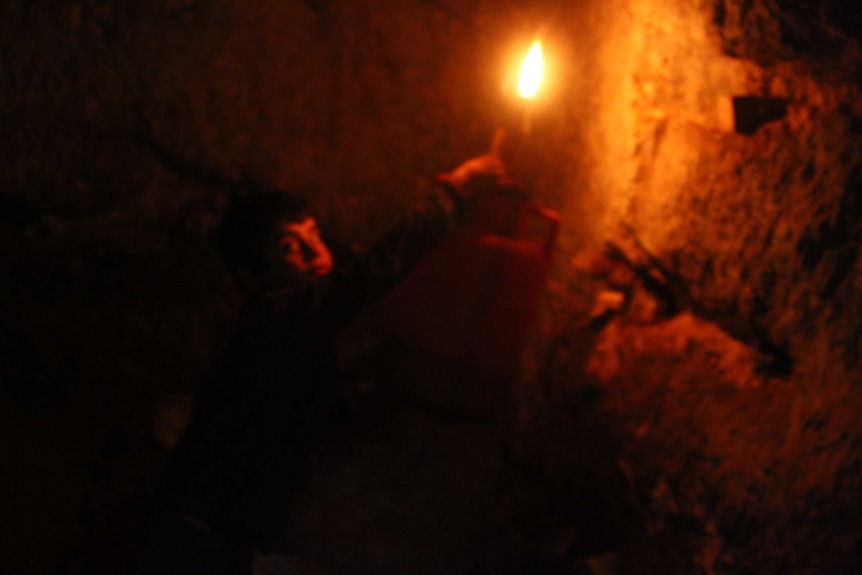 A boy holds a lamp in a cave-like room.