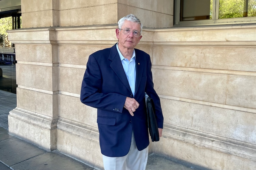 A man with grey hair wearing a suit standing outside of a court building.