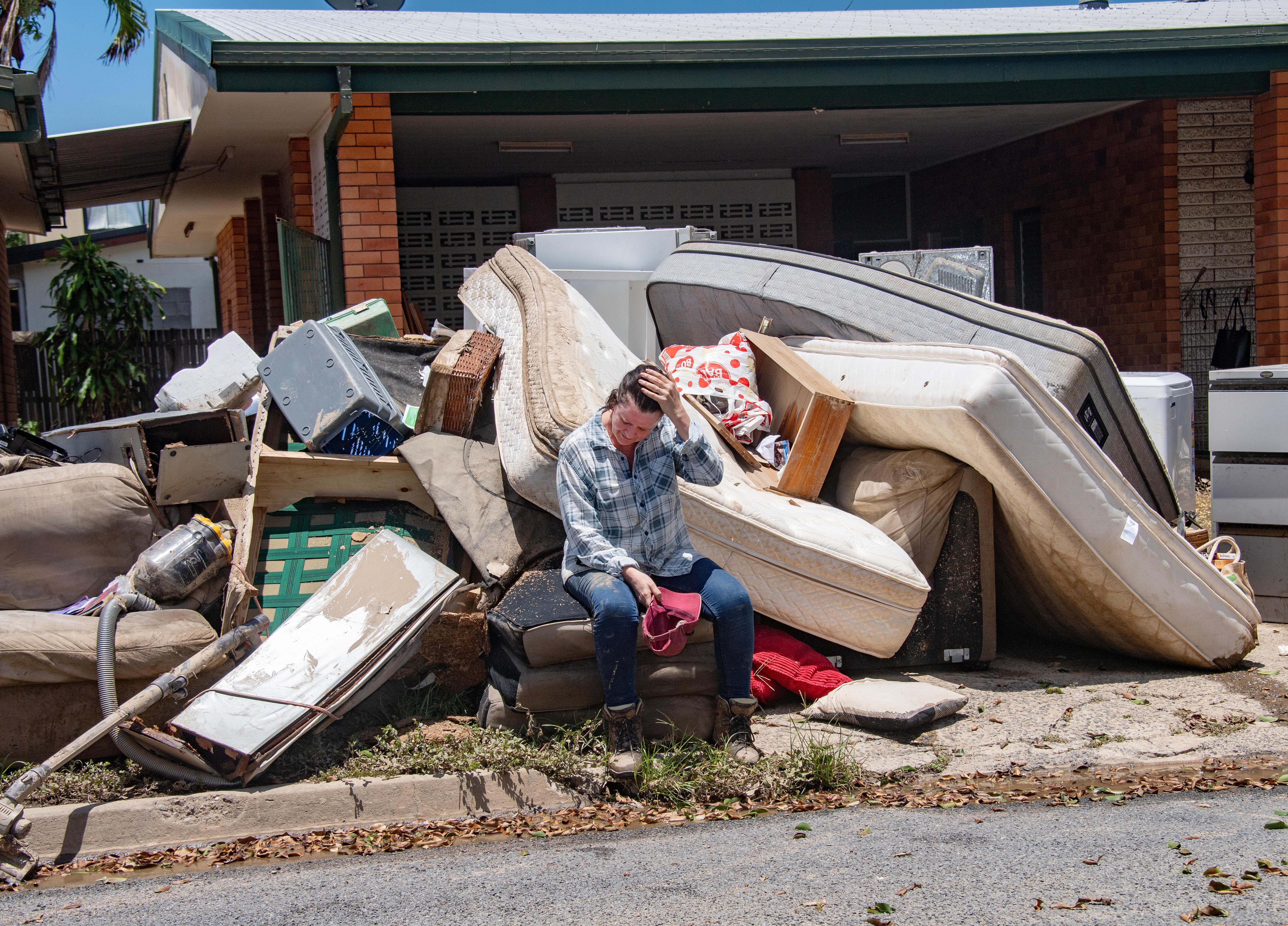 a woman sits on her curb which is laoded with flood-damaged belongings