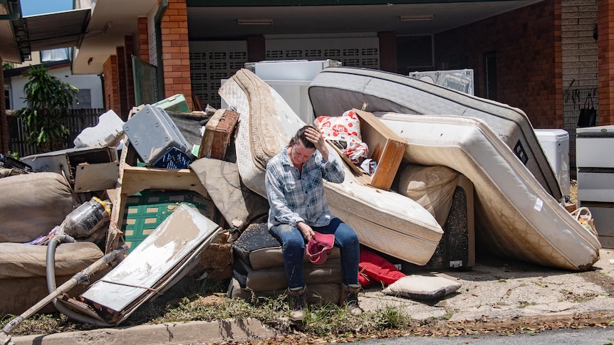 a woman sits on her curb which is laoded with flood-damaged belongings