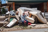 a woman sits on her curb which is laoded with flood-damaged belongings