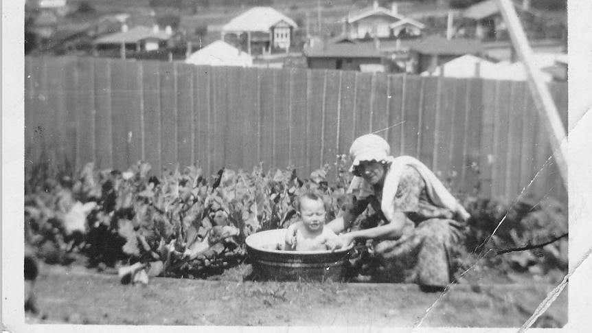 A woman giving a baby a bath in a tub in the backyard in 1924