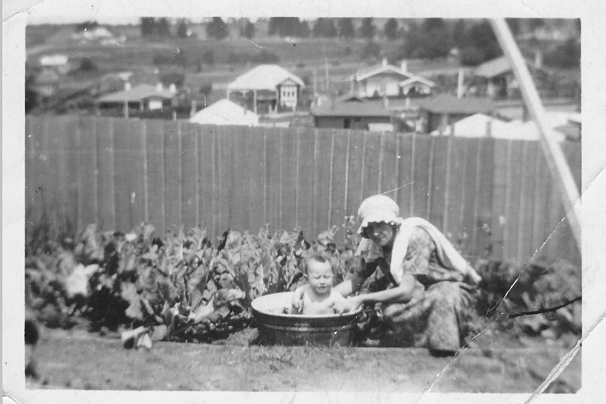 A woman giving a baby a bath in a tub in the backyard in 1924