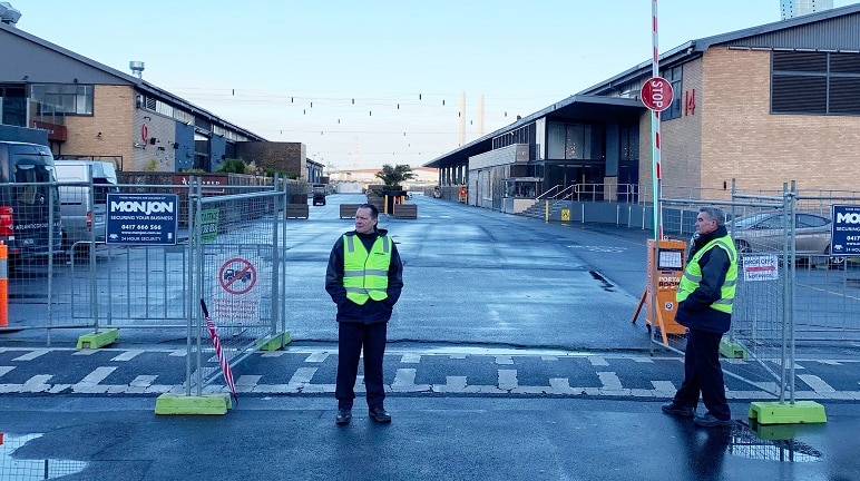 Two security guards in yellow vests stand in front of the closed-off entrance to Central Pier.