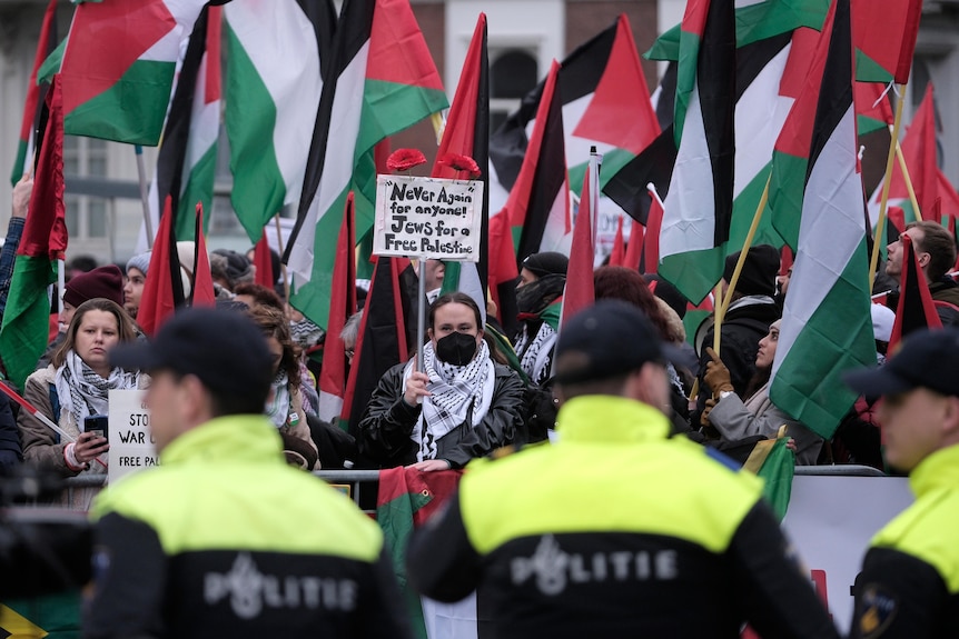 Police observe a crowd of protesters holding Free Palestine signs and holding the Palestinian flag.