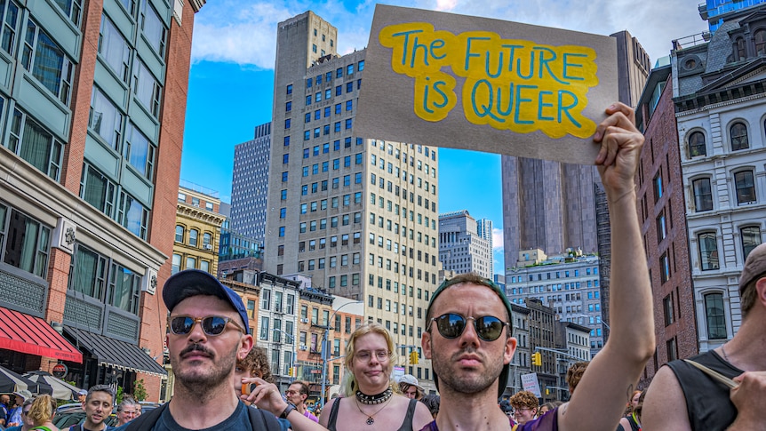 A man at a Queer Liberation march holds up a sign that reads "The future is queer"
