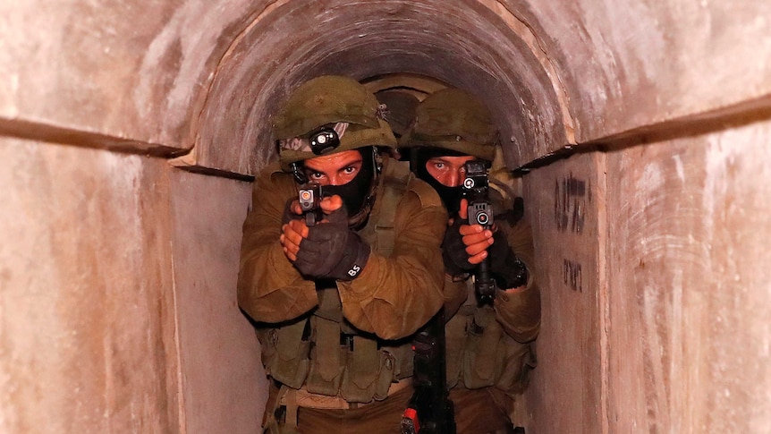 Front on view of soldiers in combat gear moving forward inside a tunnel, holding hightech weapons with cameras