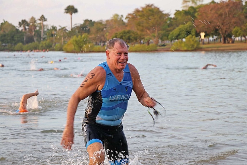 Older gentleman exiting water in triathlon branded wetsuit.