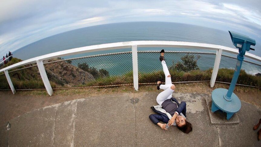 Mia Ayliffe-Chung lying on the ground near a lookout over the ocean, near Byron Bay Lighthouse.