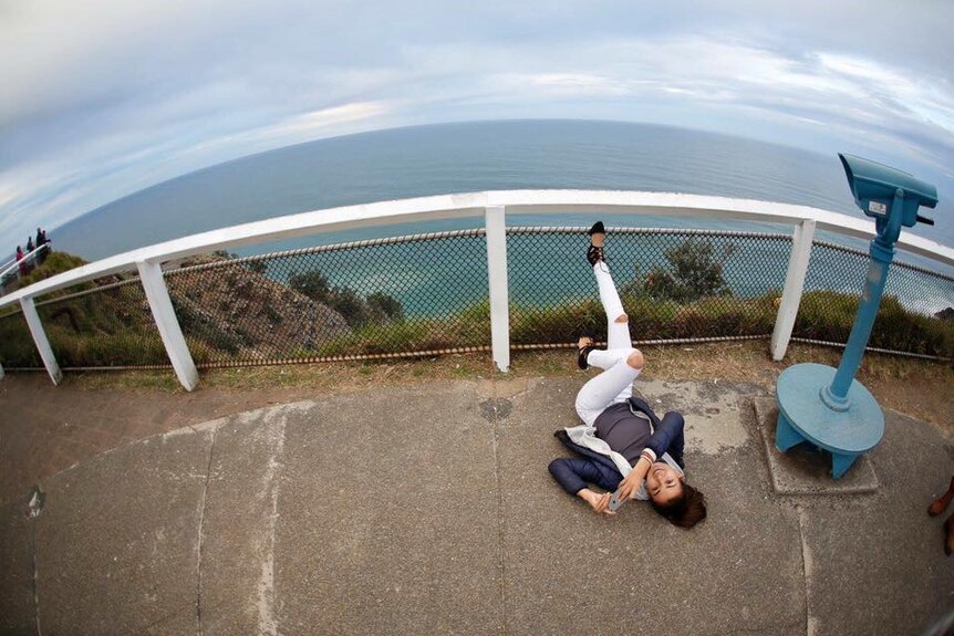 Mia Ayliffe-Chung lying on the ground near a lookout over the ocean, near Byron Bay Lighthouse.