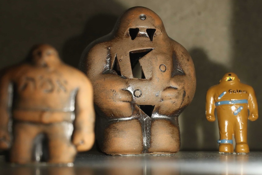 Three small figurines of the golem stand in a group, projecting their shadows onto the wall behind.