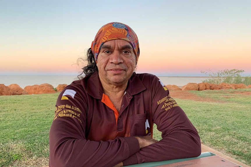 A man sits down in front of the beach staring into the camera