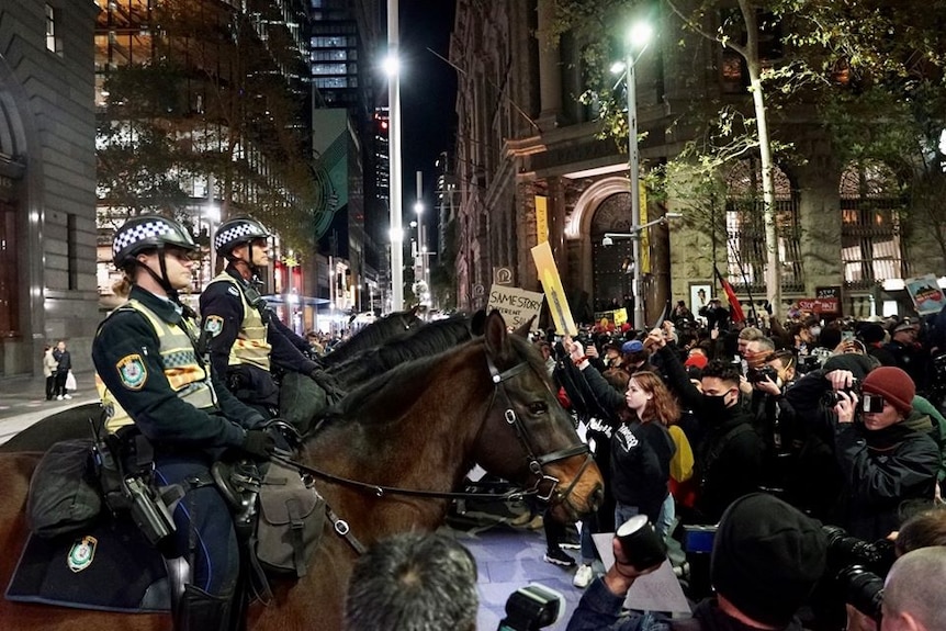 Police on horseback stand face to face with crowd of protesters in Martin Place