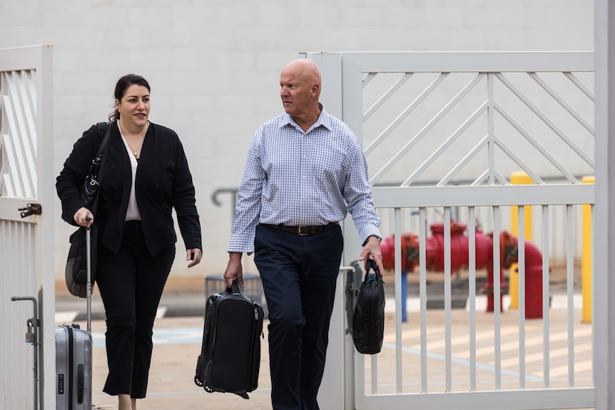 A man and a woman, both lawyers, arriving at a courthouse carrying briefcases.  