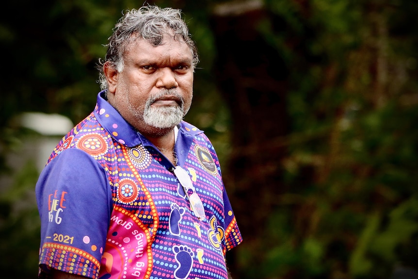 an aboriginal man wearing a purple collared shirt with indigenous prints
