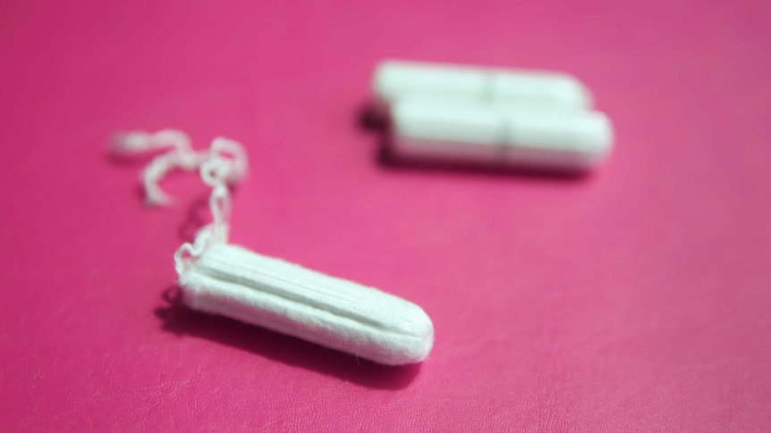 Three tampons sit on a pink surface.